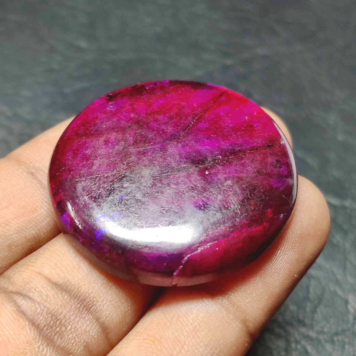 Cabochons4sale round purple dyed labradorite gemstone cabochon with a polished translucent finish held in a hand