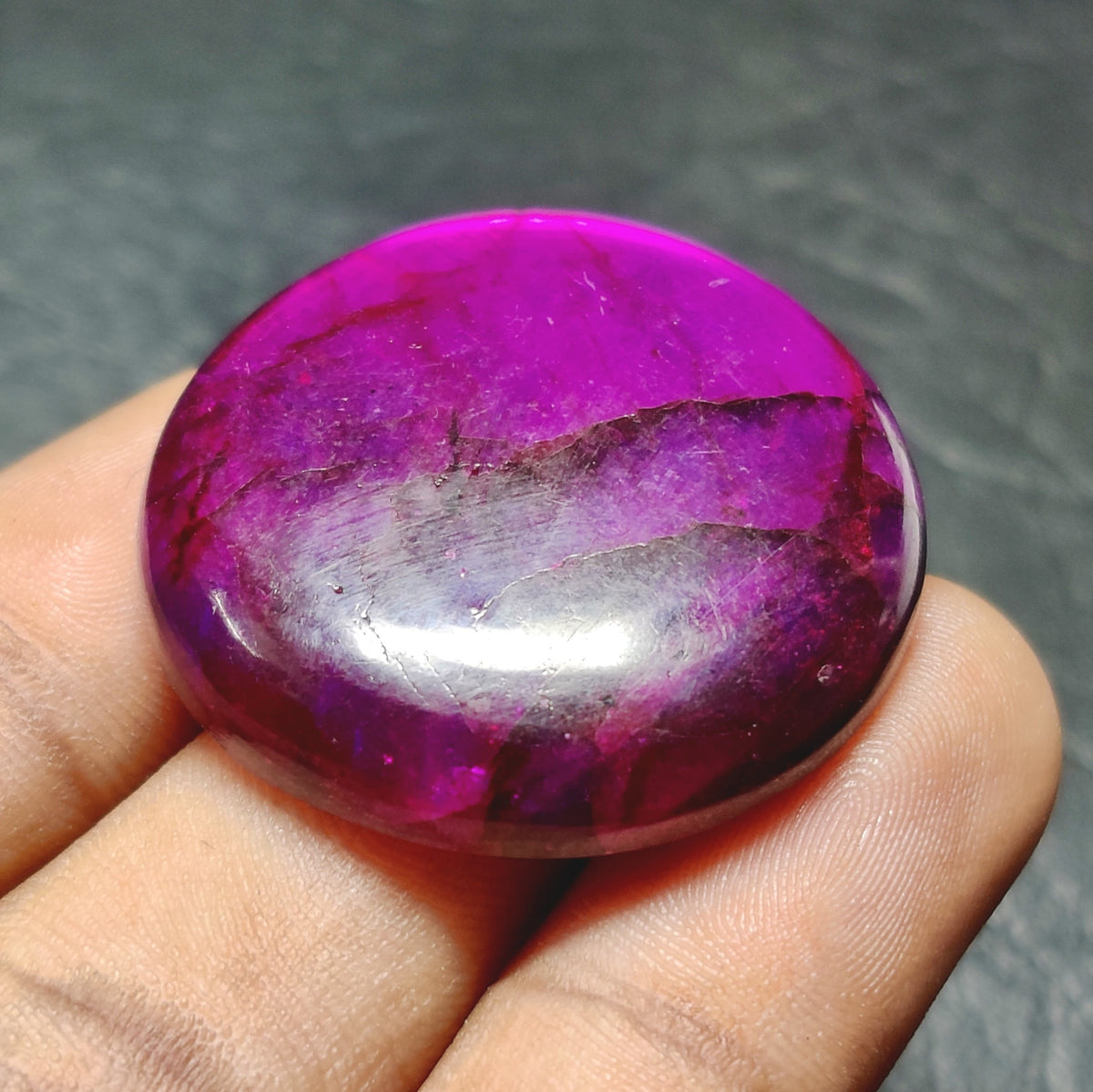 Cabochons4sale round purple dyed labradorite cabochon gemstone with a translucent finish held between fingers