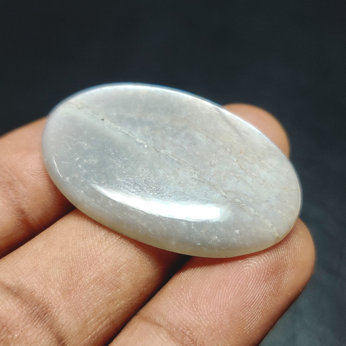 Cabochons4sale oval grey moonstone cabochon with a translucent finish held between fingers