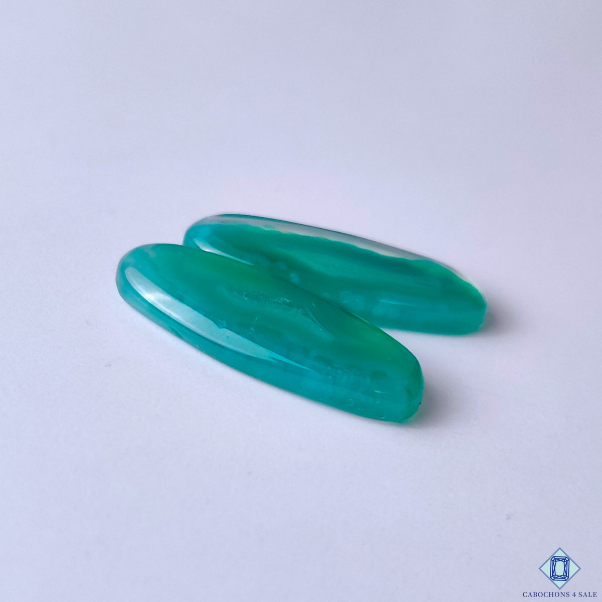cabochons4sale, oval green banded agate cabochons featuring soft white layers, organic curved markings and a smooth polished gemstone surface held between fingers