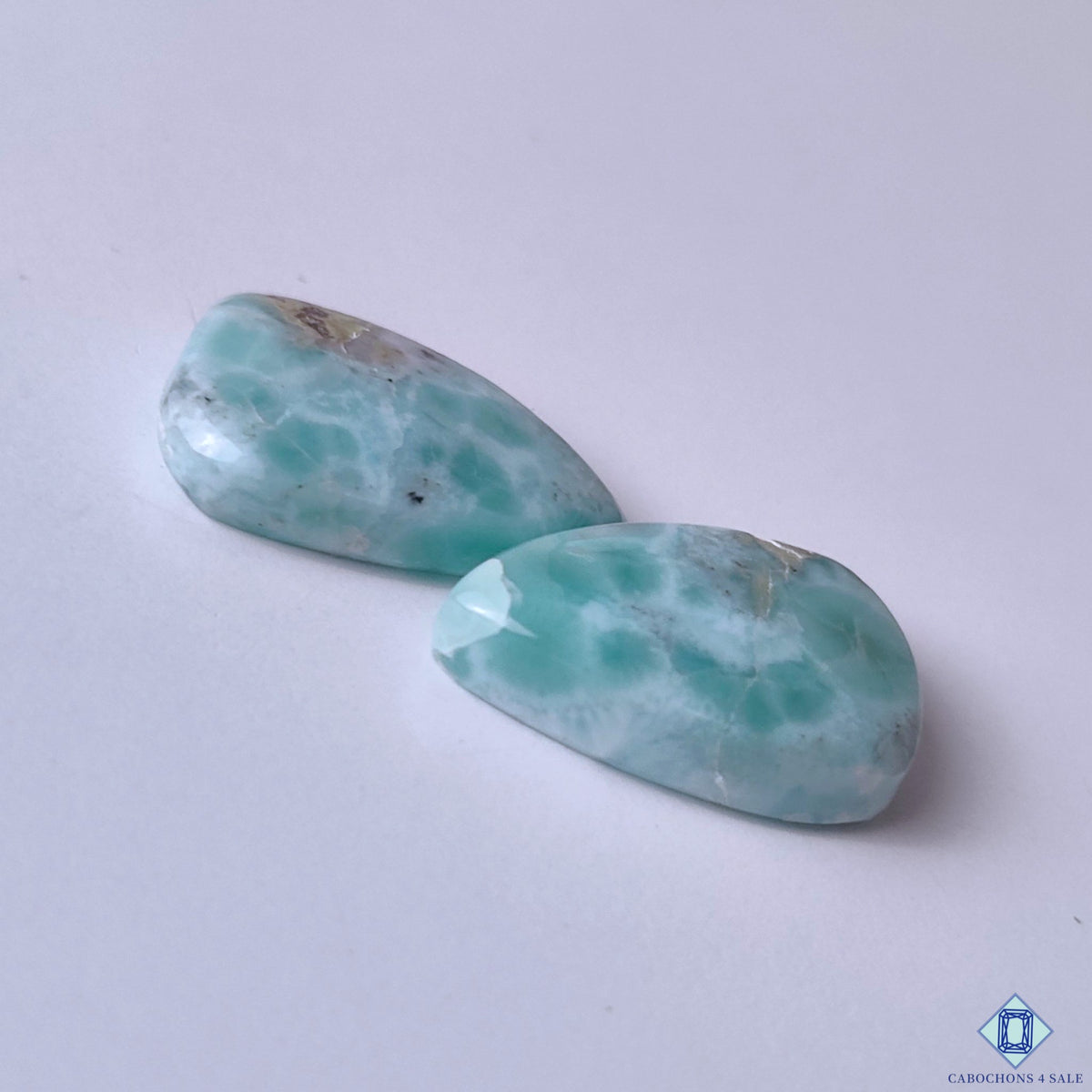 cabochons4sale, white and blue larimar pear cabochons featuring tropical ocean-inspired markings, soft color variation and distinctive natural gemstone character held between fingers