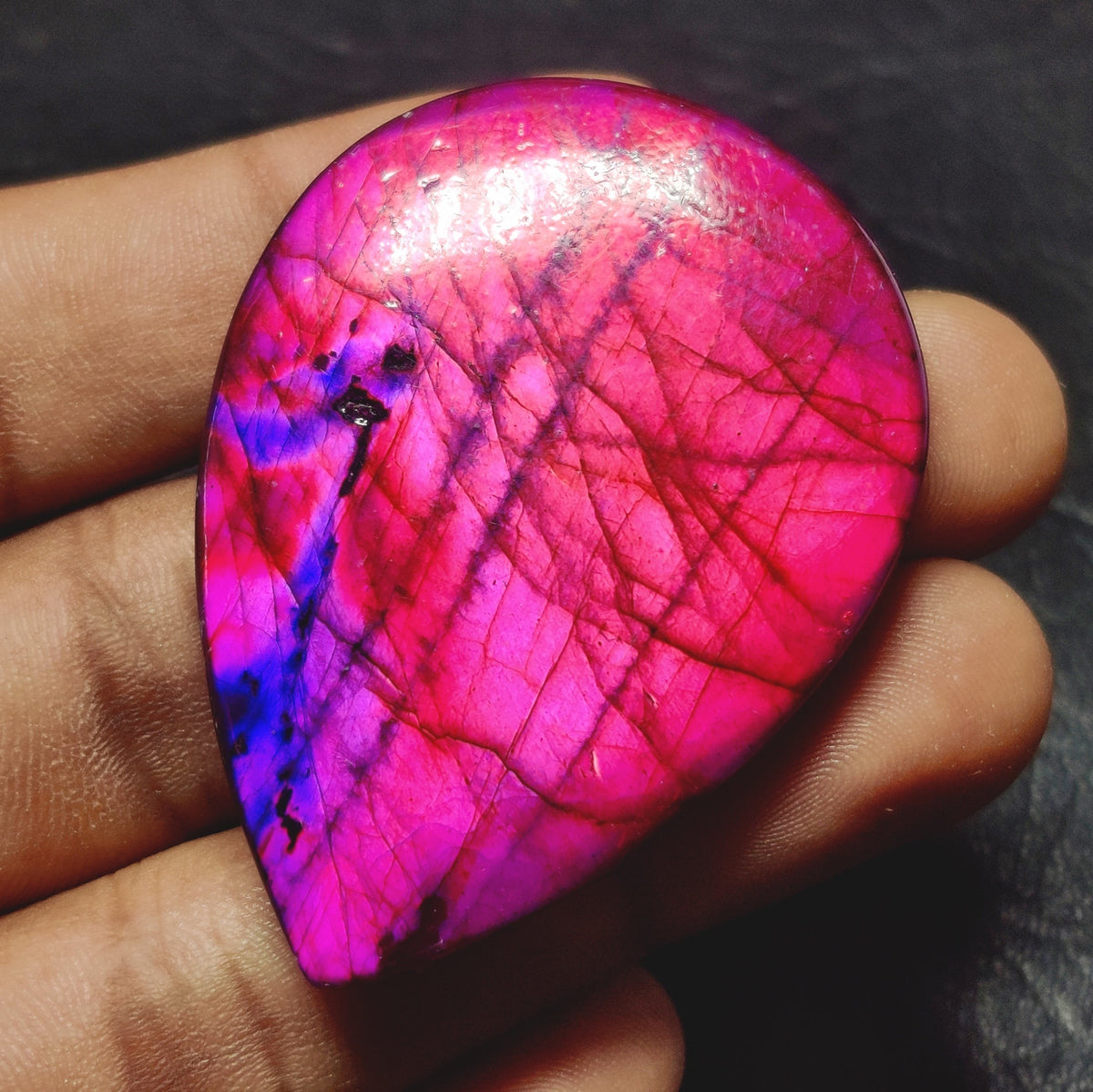 Cabochons4sale pear-shaped translucent dyed labradorite gemstone in vibrant purple held in a hand