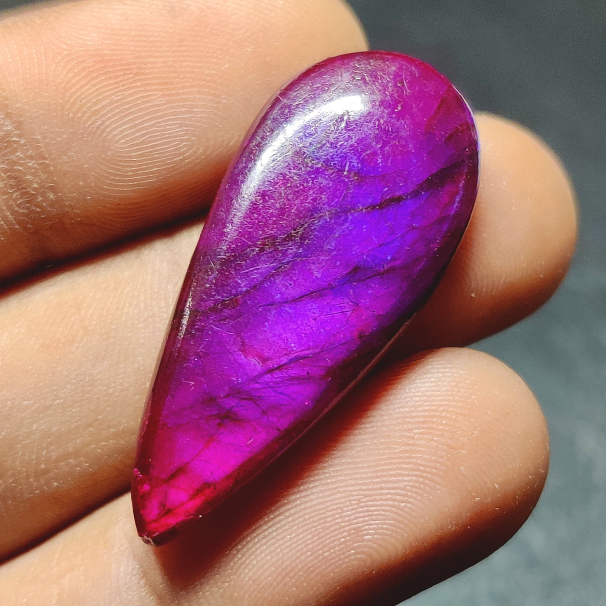 Cabochons4sale purple dyed labradorite pear cabochon gemstone with translucent finish held in fingers