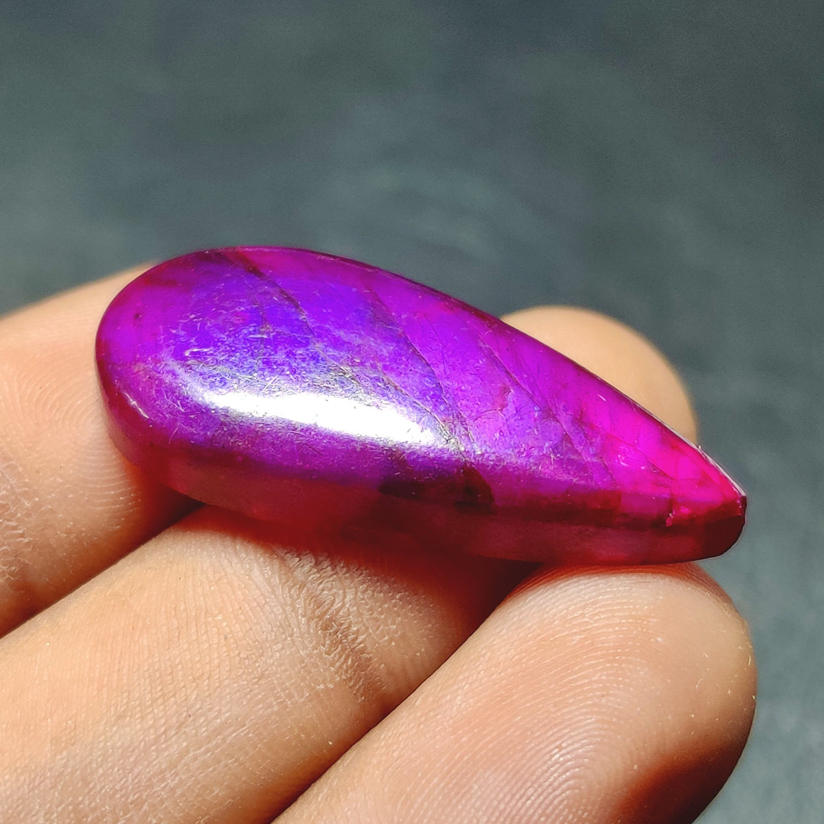 Cabochons4sale purple dyed labradorite pear cabochon gemstone with a translucent finish held between fingers