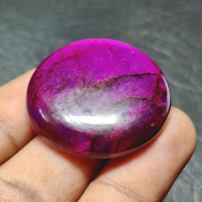 Cabochons4sale round purple dyed labradorite cabochon gemstone with a translucent finish held between fingers