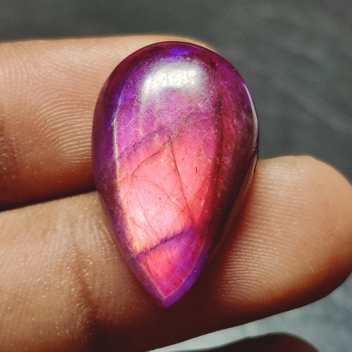 Cabochons4sale pear-shaped translucent purple dyed labradorite gemstone held between fingers