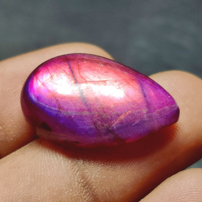 Cabochons4sale purple dyed labradorite pear cabochon gemstone with a translucent finish held in fingers