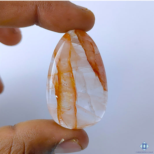 Cabochons4sale translucent pear-shaped fire quartz gemstone with red inclusions held between fingers