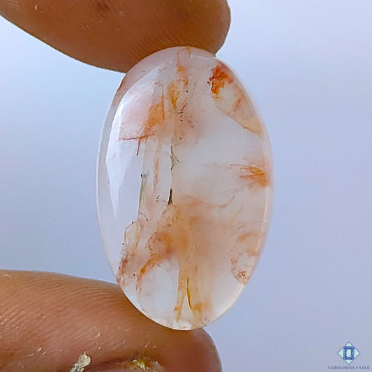 Cabochons4sale oval fire quartz cabochon with translucent red inclusions, 26x16x7mm gemstone held between fingers.
