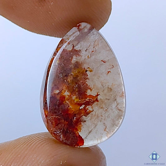Cabochons4sale pear-shaped translucent fire quartz gemstone with red inclusions held between fingers