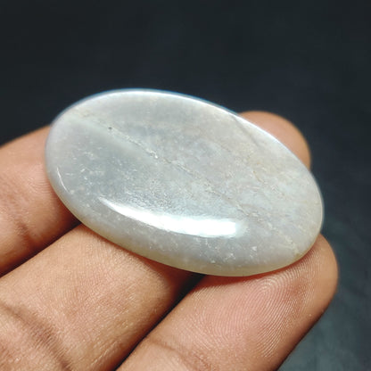 Cabochons4sale oval grey moonstone cabochon with a translucent finish held between fingers