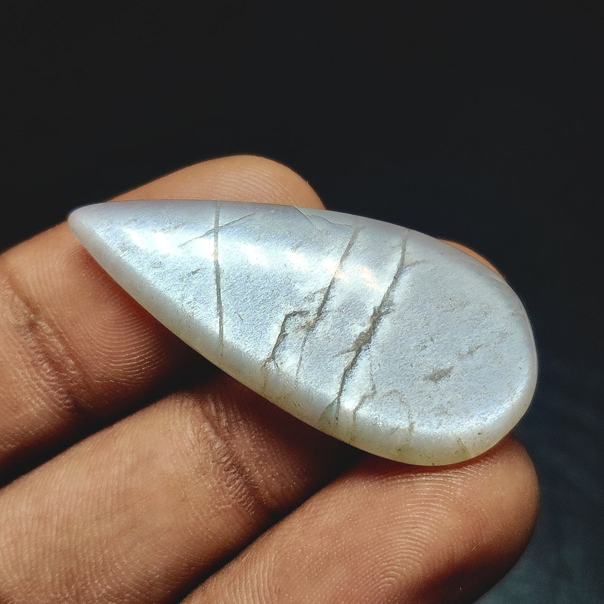 Cabochons4sale grey moonstone pear cabochon gemstone with a translucent finish held between fingers