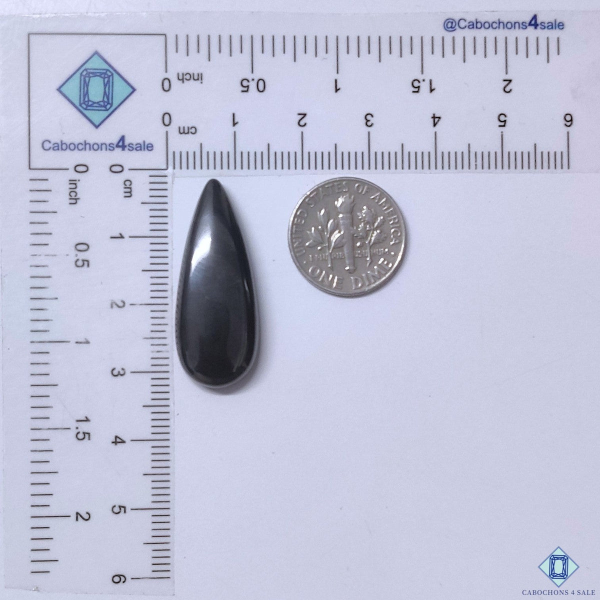 Cabochons4sale grey gun metal pear cabochon gemstone measuring 31x12x5mm with an opaque finish next to a US dime.