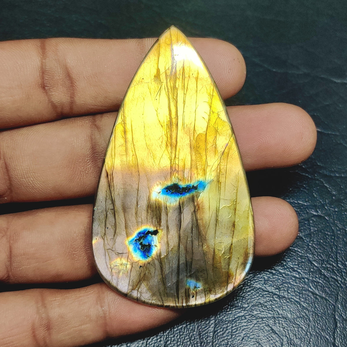 Cabochons4sale pear-shaped yellow labradorite cabochon with blue flashes held in a hand