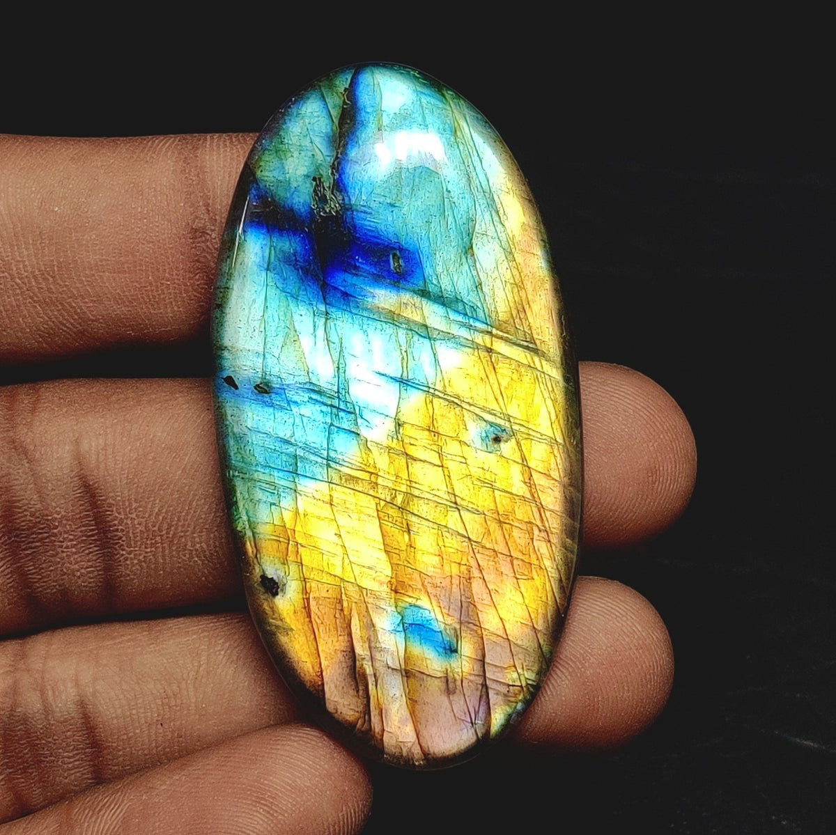 Cabochons4sale oval labradorite cabochon with vibrant blue and yellow iridescent flashes held in a hand