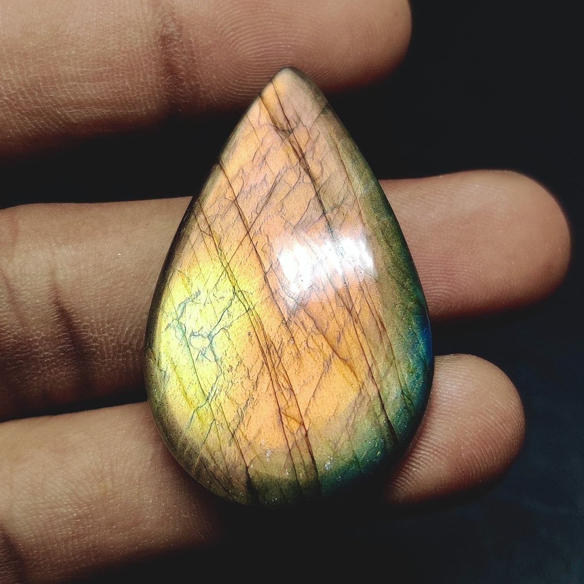 Cabochons4sale pear-shaped labradorite cabochon with iridescent orange and green flashes held between fingers