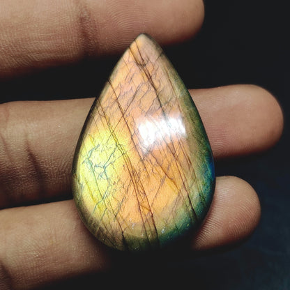 Cabochons4sale pear-shaped labradorite cabochon with iridescent orange and green flashes held between fingers