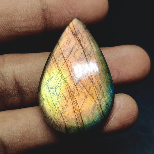 Cabochons4sale pear-shaped labradorite cabochon with iridescent orange and green flashes held between fingers