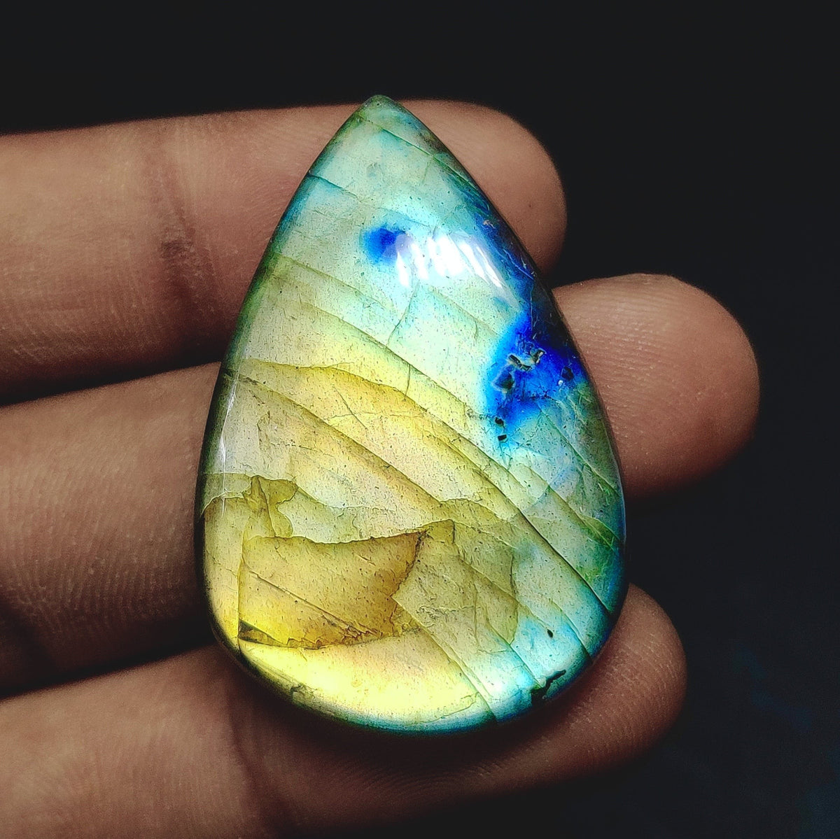 Cabochons4sale pear-shaped labradorite cabochon with iridescent blue and yellow flashes held in a hand