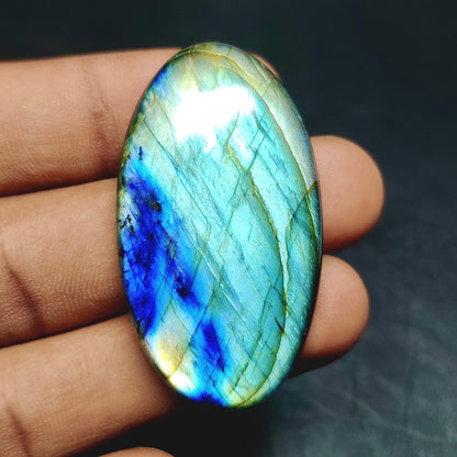 Cabochons4sale oval labradorite cabochon featuring vibrant blue and green iridescent flashes held in a hand