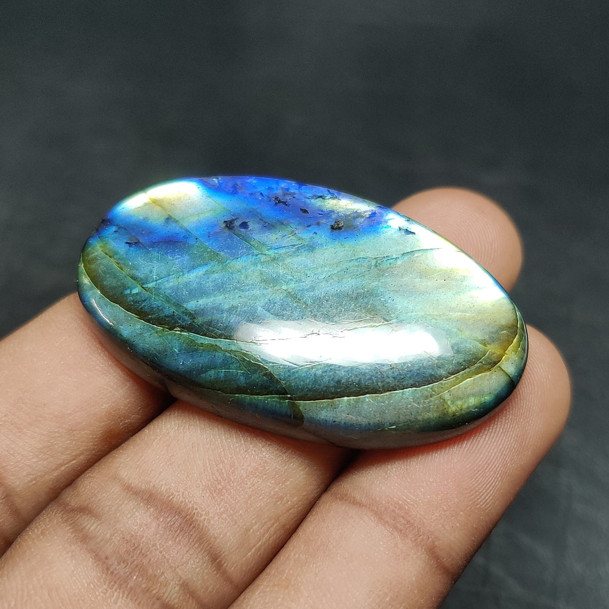 Cabochons4sale oval labradorite cabochon with iridescent blue and green flashes held in a hand