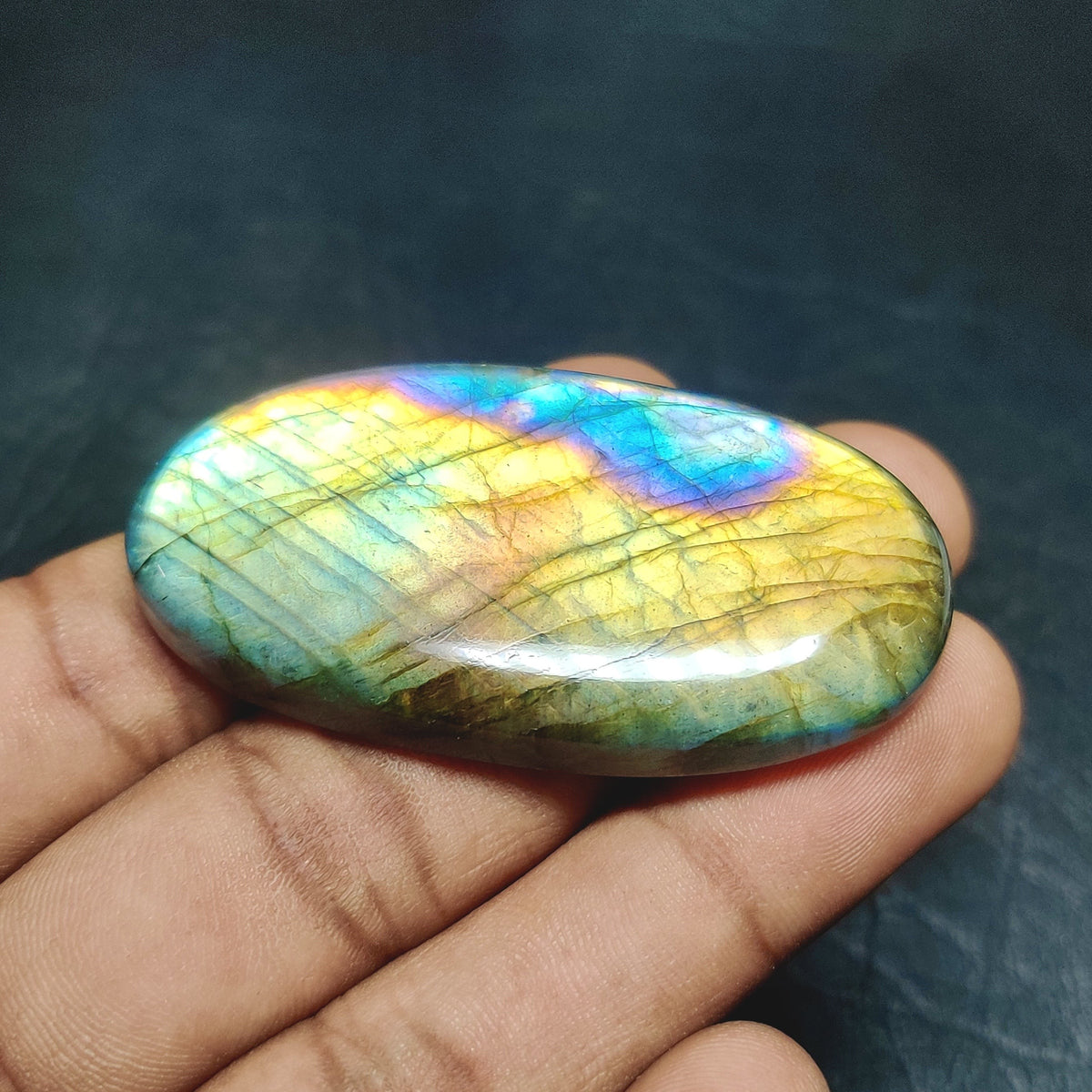 Cabochons4sale oval labradorite gemstone with iridescent blue and yellow flashes held in a hand