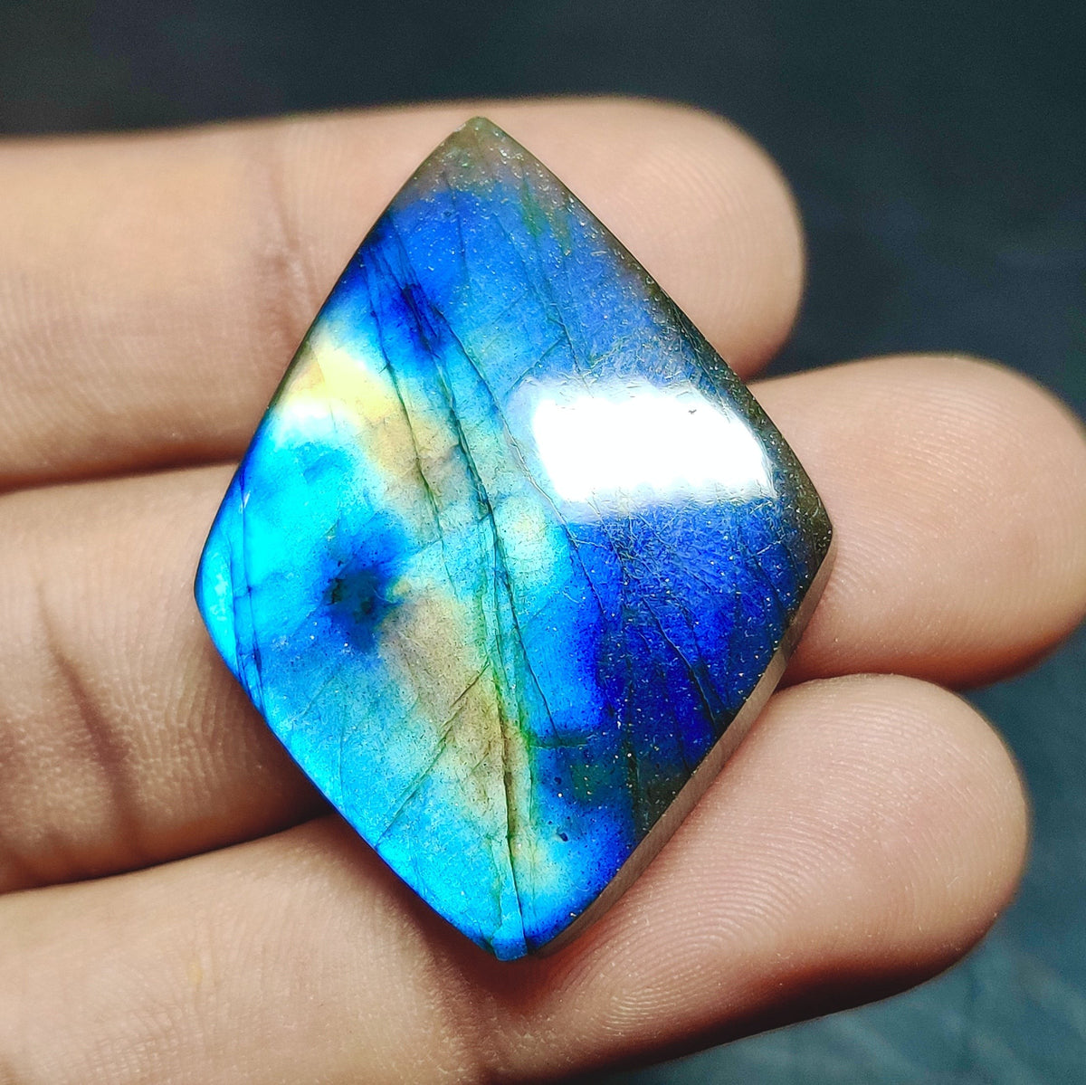 Cabochons4sale marquise cut labradorite gemstone with vibrant blue and yellow iridescent flash held in fingers