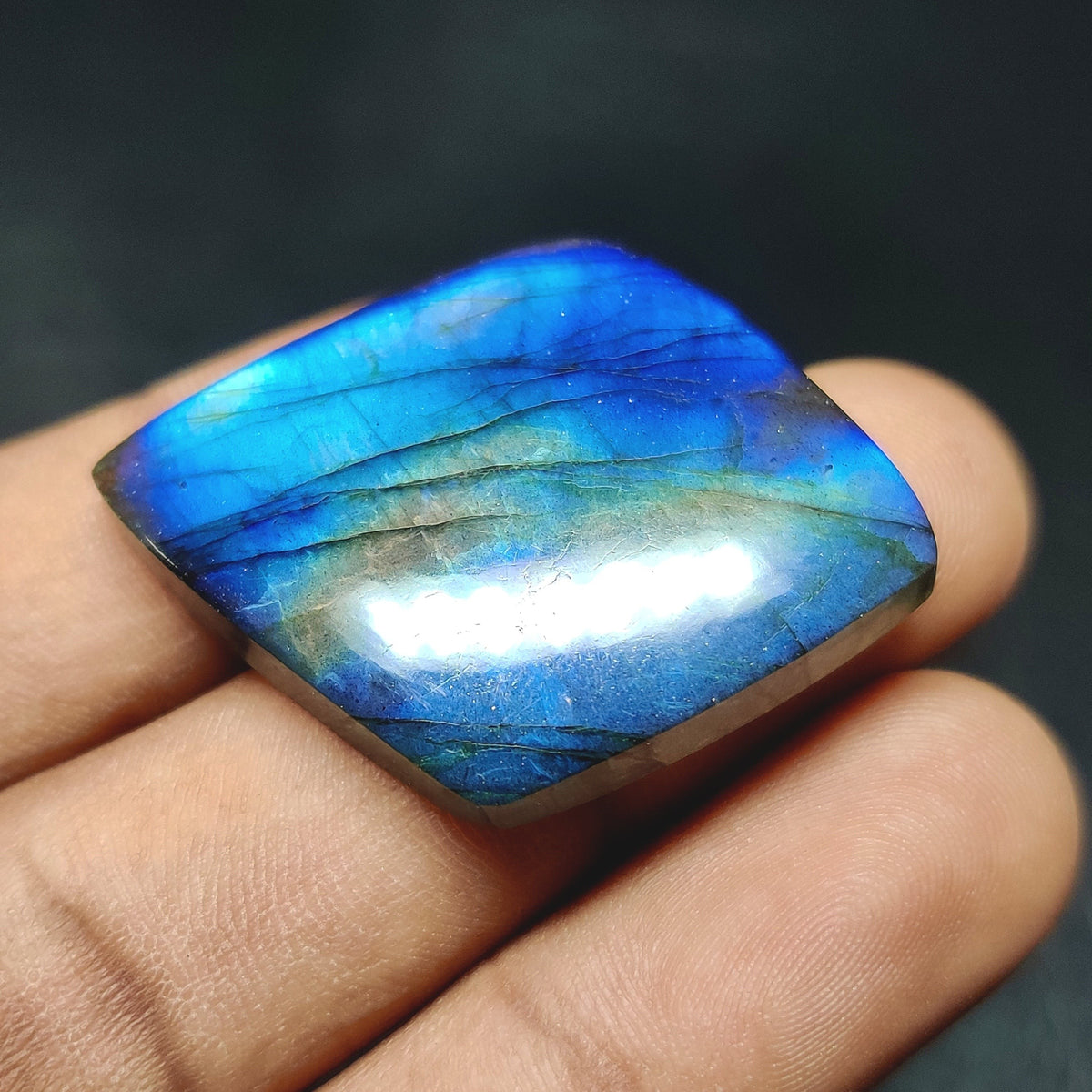 Cabochons4sale marquise-cut labradorite gemstone with translucent blue and green iridescent flash held in fingers.