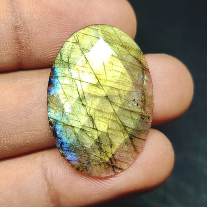 Cabochons4sale oval rose cut labradorite gemstone with translucent yellow and blue iridescent flashes held in fingers