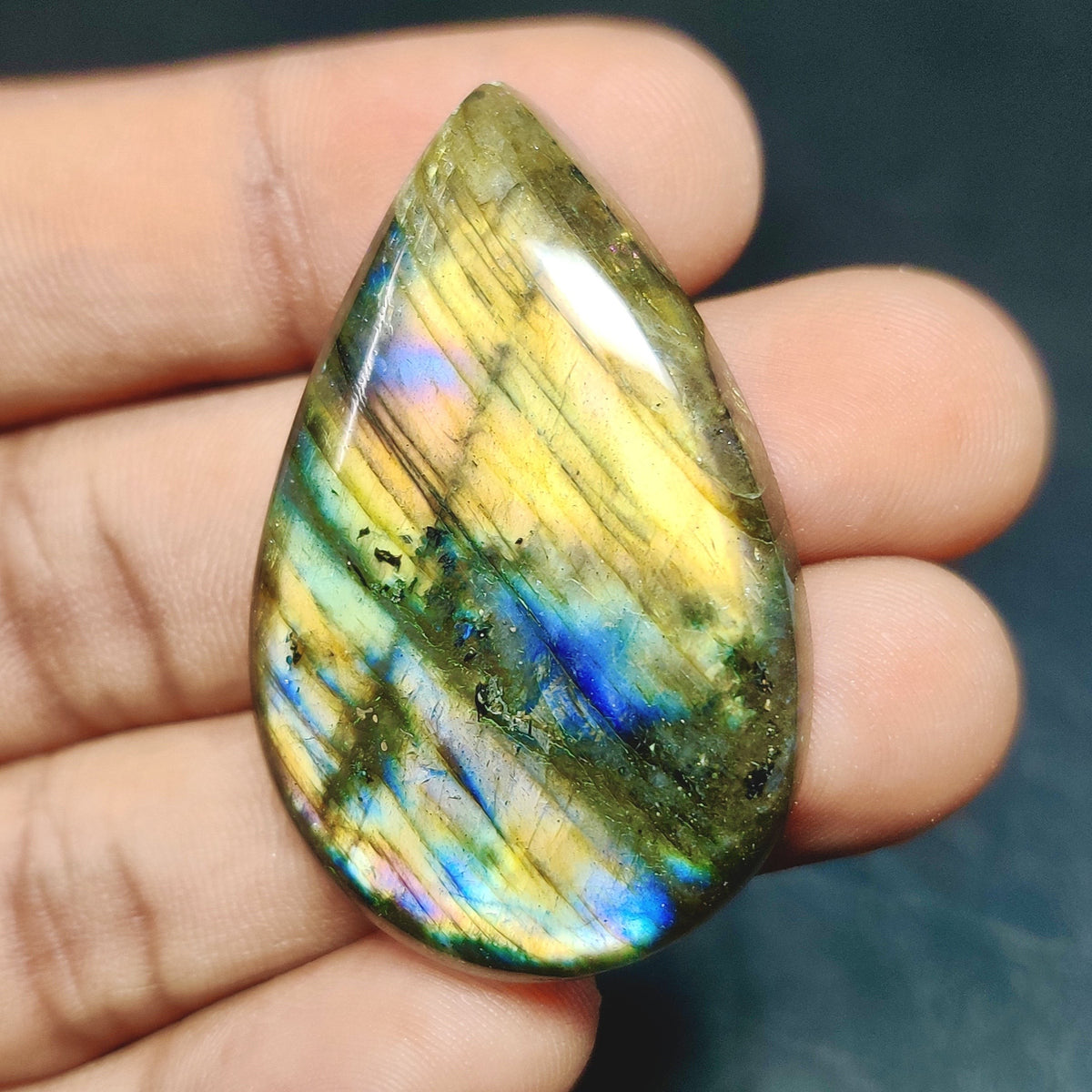 Cabochons4sale pear-shaped labradorite cabochon with iridescent blue and yellow flashes held in a hand