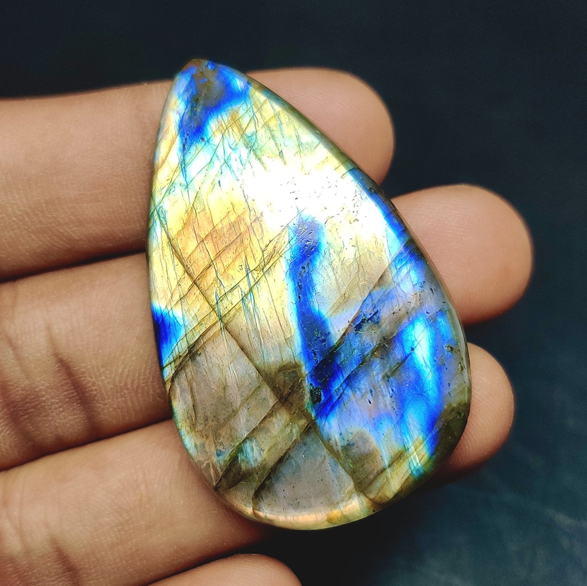 Cabochons4sale pear-shaped labradorite gemstone with iridescent blue and gold flashes held in a hand