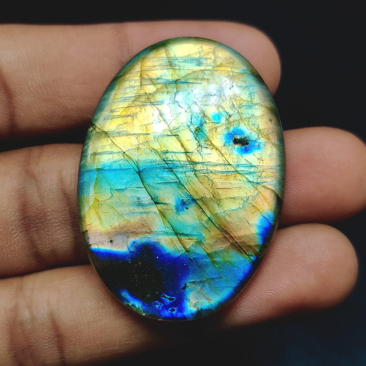 Cabochons4sale oval labradorite gemstone with iridescent blue and yellow flashes held in a hand