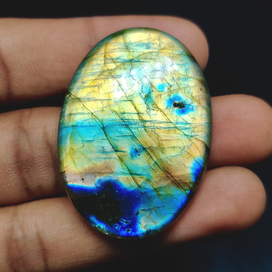 Cabochons4sale oval labradorite gemstone with iridescent blue and yellow flashes held in a hand