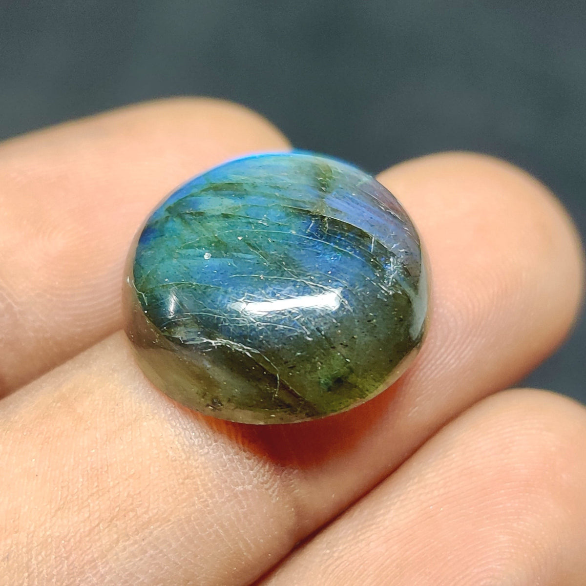 Cabochons4sale round translucent labradorite gemstone with blue iridescent flash held between fingers
