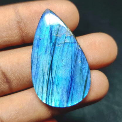 Cabochons4sale pear-shaped translucent labradorite gemstone with vibrant blue flash held in fingers