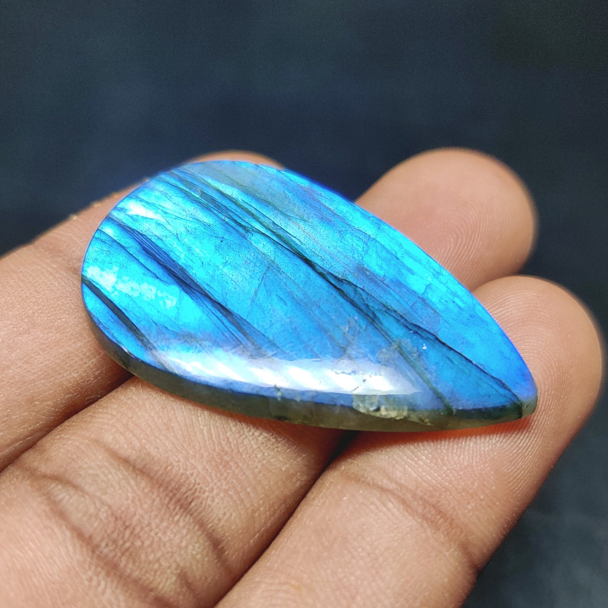 Cabochons4sale pear-shaped translucent labradorite gemstone with vibrant blue flash held in a hand