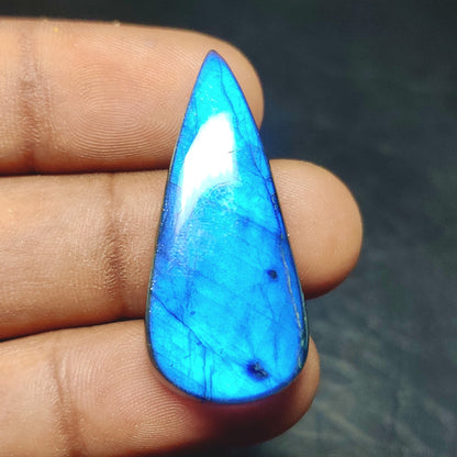 Cabochons4sale pear-shaped translucent labradorite gemstone with vibrant blue flash held between fingers