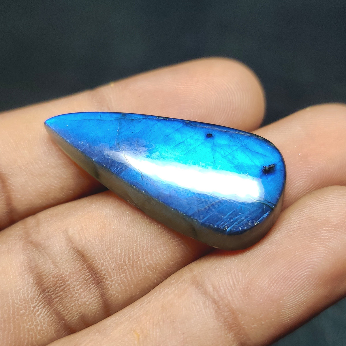 Cabochons4sale pear-shaped translucent labradorite gemstone with vibrant blue flash held in a hand