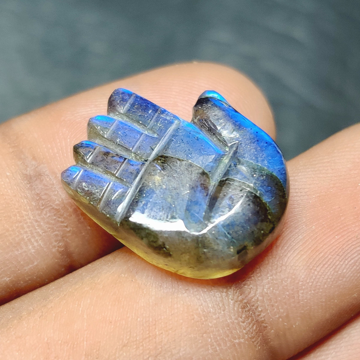 Cabochons4sale translucent blue labradorite gemstone carved into a hamsa hand shape held on a finger