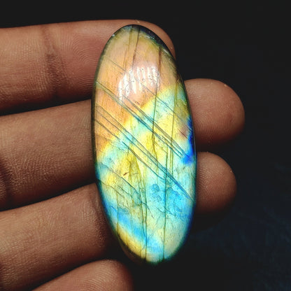 Cabochons4sale oval labradorite cabochon with iridescent blue and yellow flashes held in a hand
