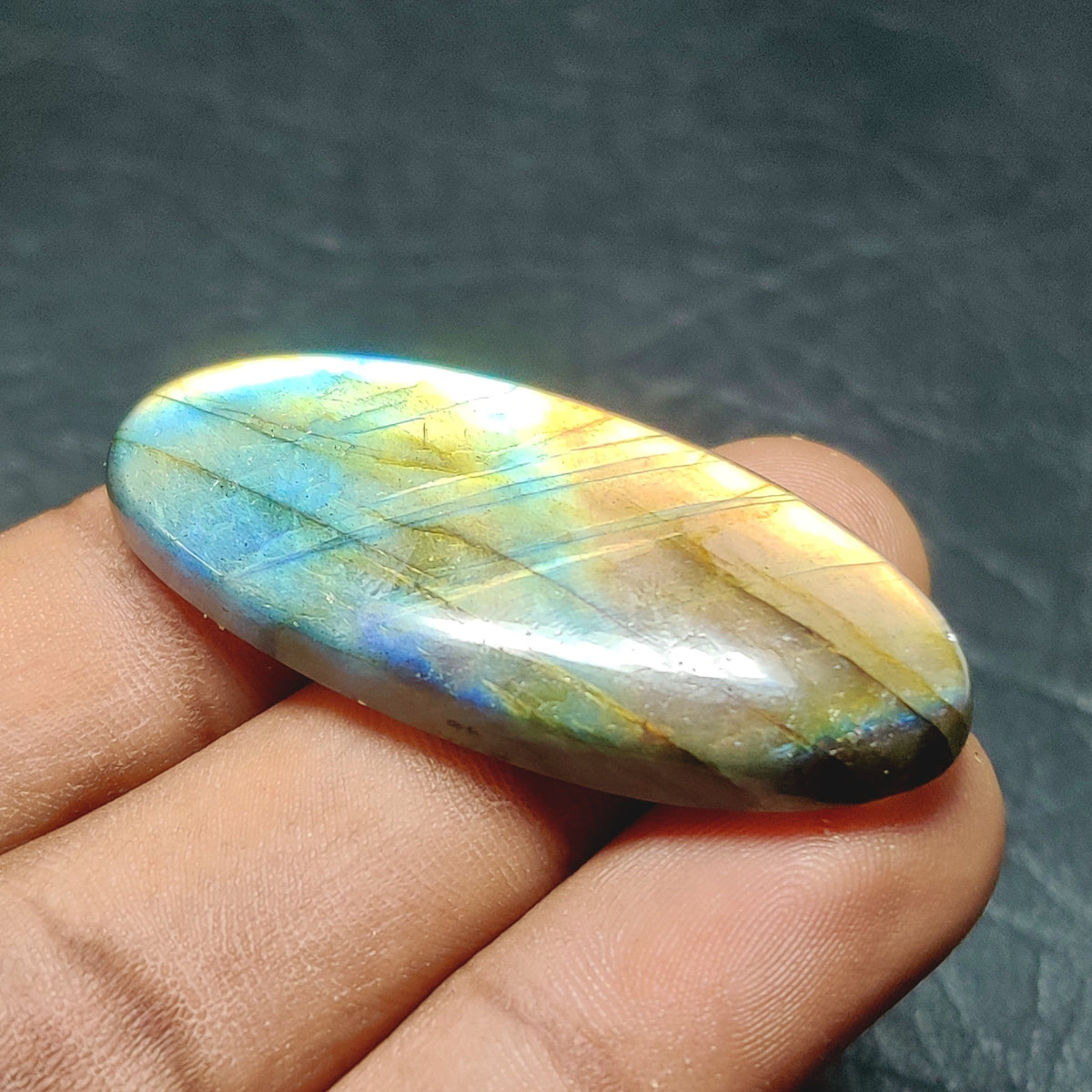 Cabochons4sale oval labradorite cabochon with iridescent blue and gold flashes held in a hand