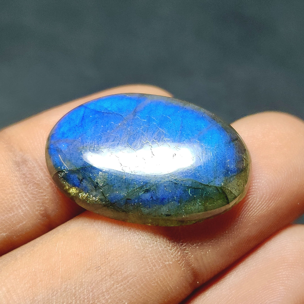 Cabochons4sale oval labradorite gemstone with vibrant blue flash and translucent finish held between fingers