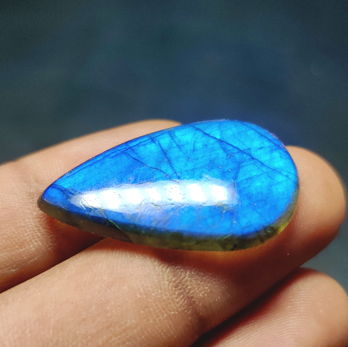Cabochons4sale pear-shaped translucent labradorite gemstone with vibrant blue flash held between fingers