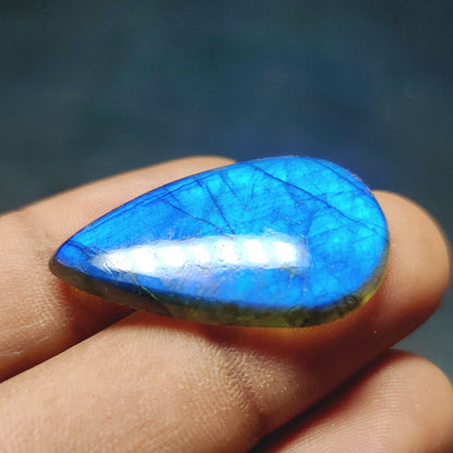 Cabochons4sale pear-shaped translucent labradorite gemstone with vibrant blue flash held between fingers