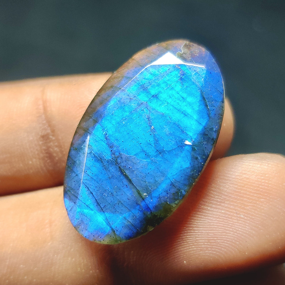 Cabochons4sale oval translucent labradorite gemstone with vibrant blue flash held between fingers