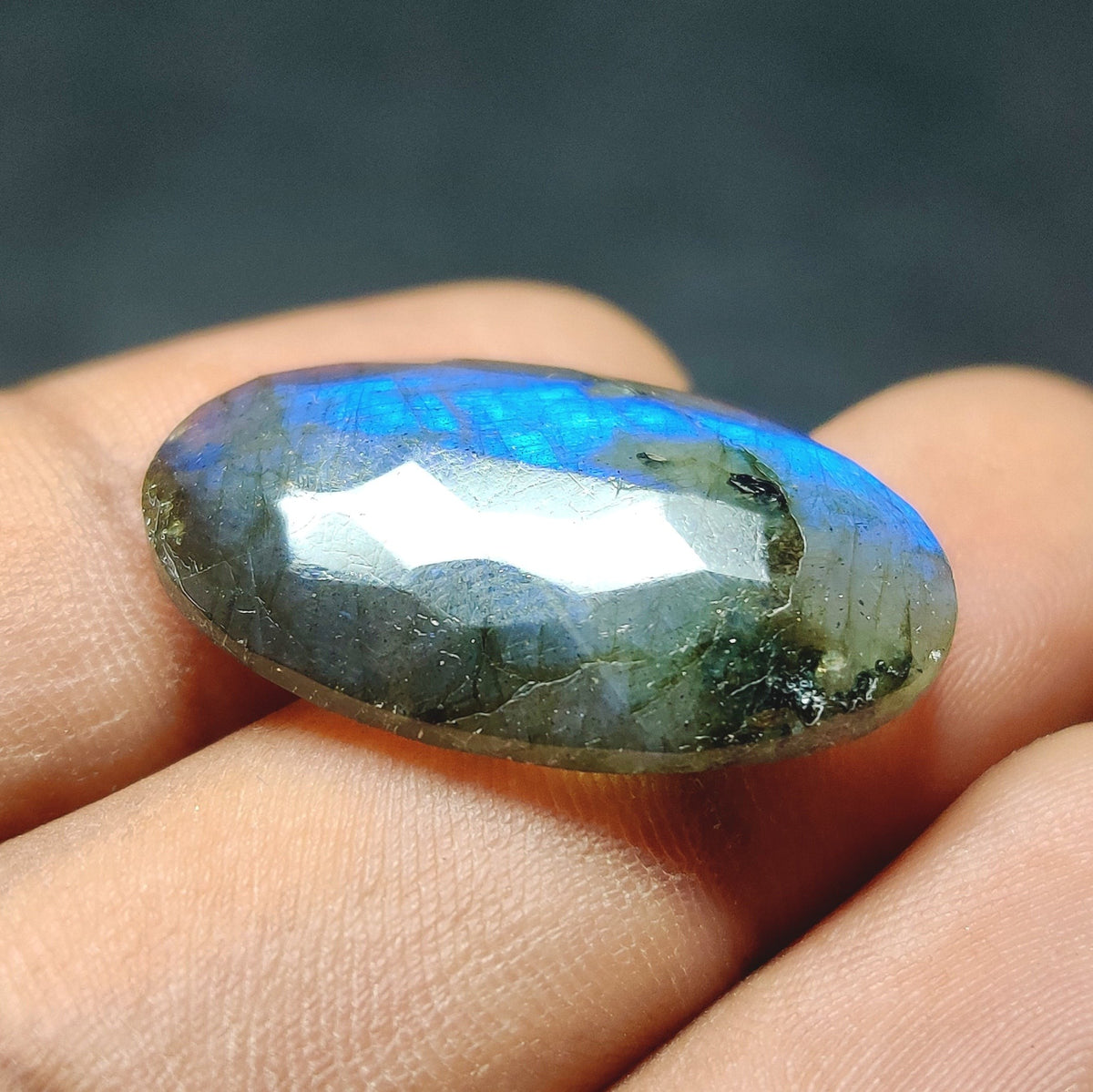Cabochons4sale oval labradorite gemstone with blue iridescent flash held between fingers