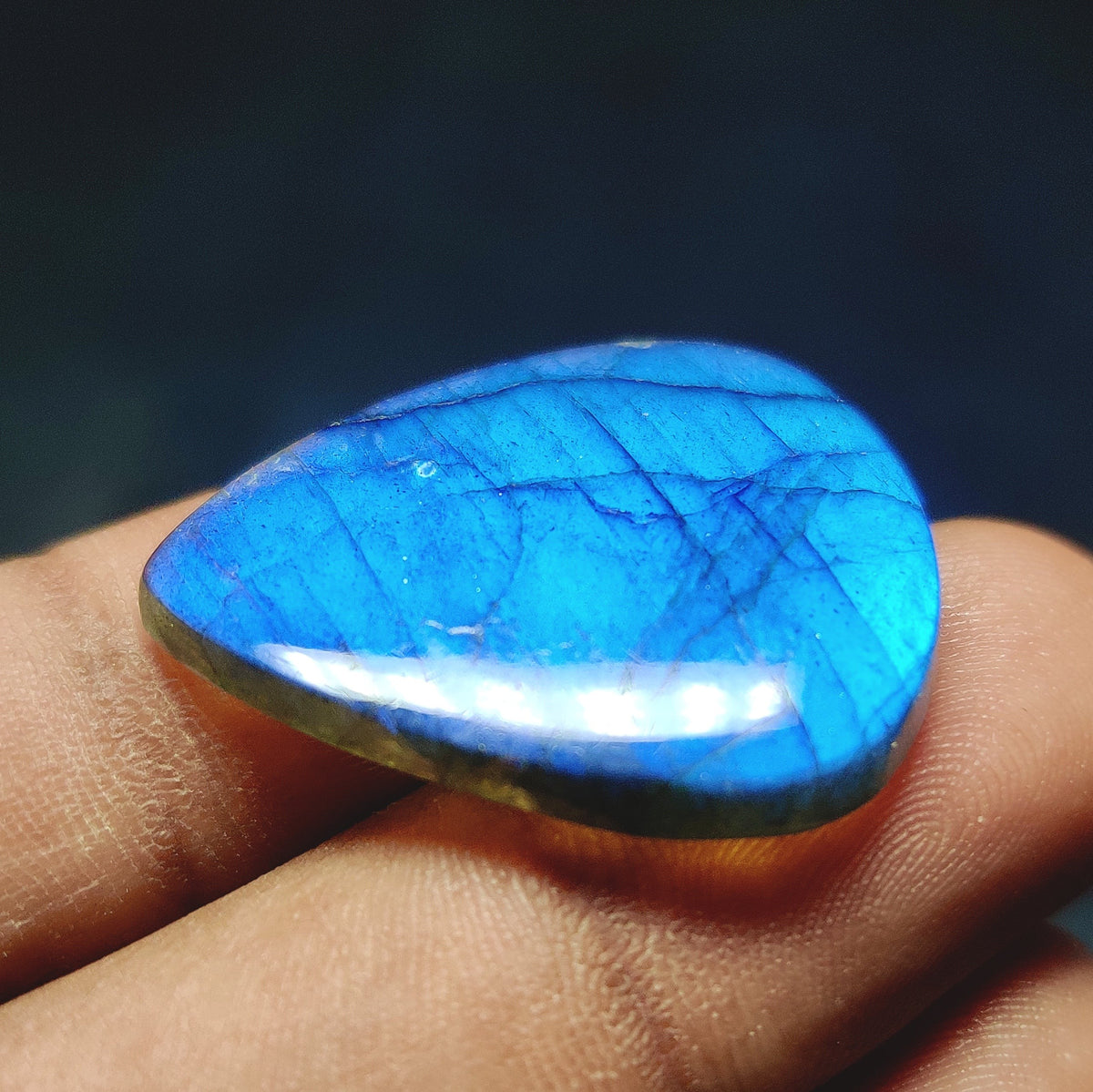 Cabochons4sale pear-shaped translucent labradorite gemstone with vibrant blue flash held between fingers