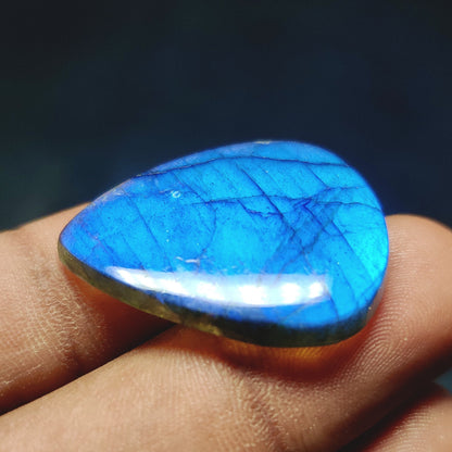 Cabochons4sale pear-shaped translucent labradorite gemstone with vibrant blue flash held between fingers