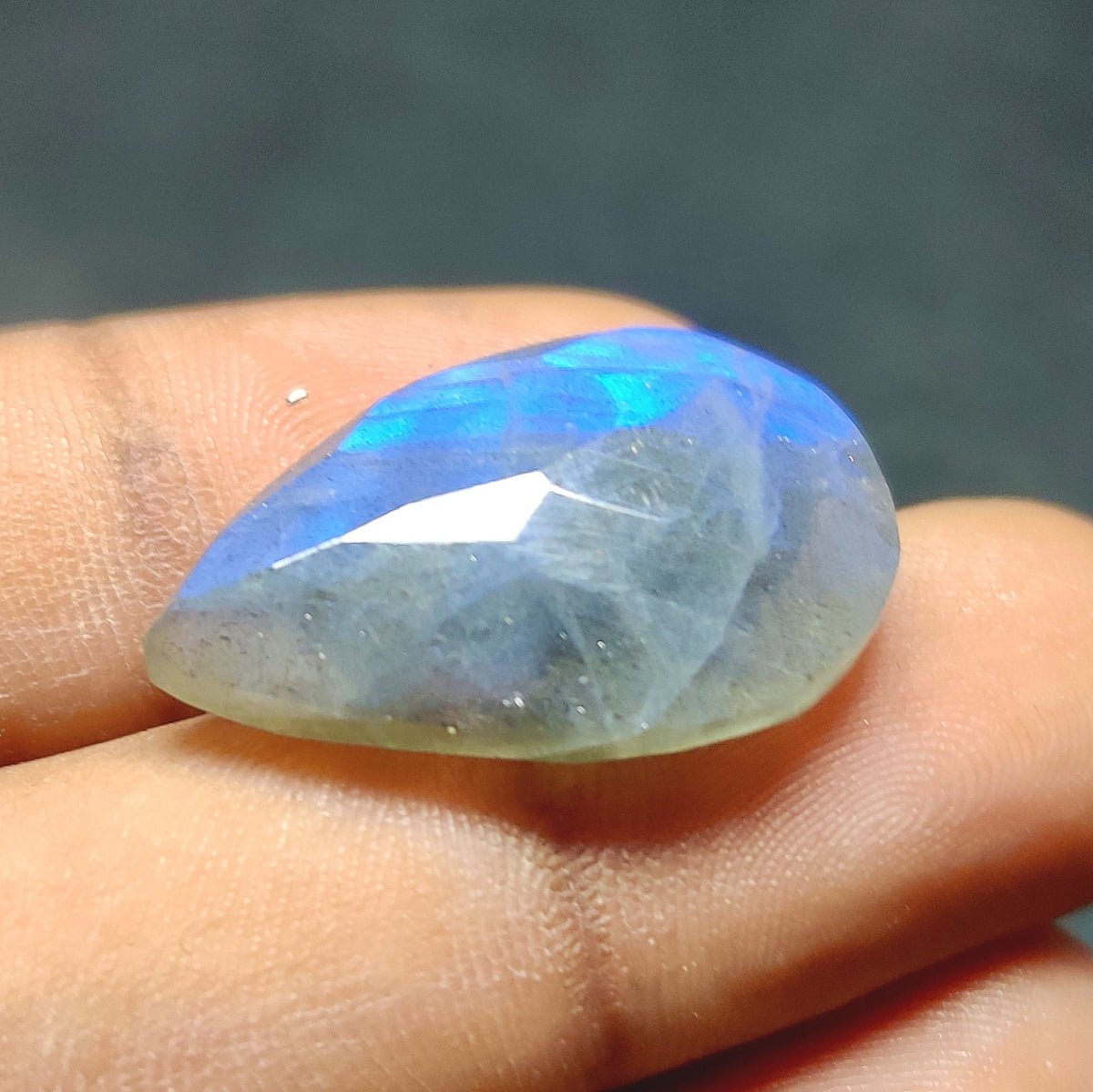 Cabochons4sale pear-shaped faceted labradorite gemstone with translucent blue flash held between fingers