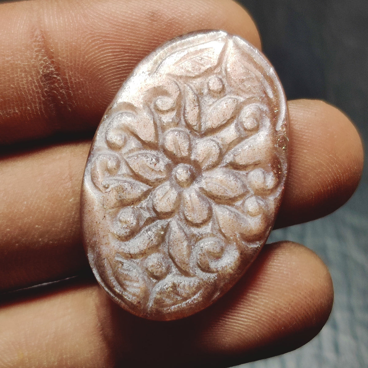 Cabochons4sale oval peach moonstone gemstone with intricate floral carving held between fingers